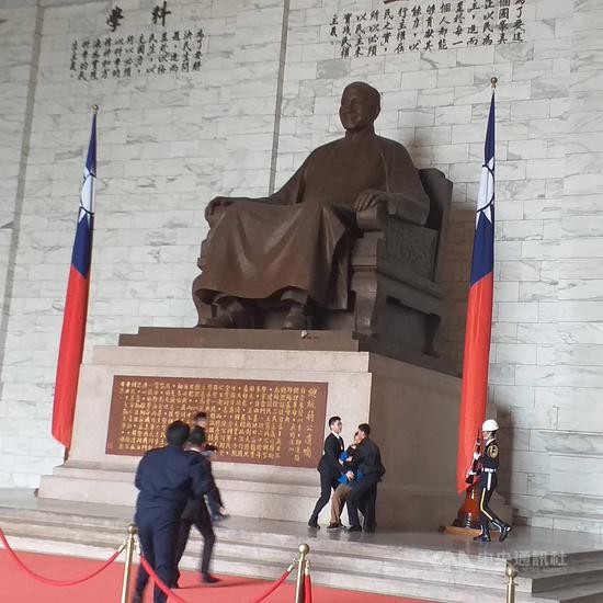 臺灣國辦公室主任陳峻涵(藍衣者)多次到中正紀念堂潑漆、抗議,他10日中午又趁機持兩袋紅墨水到場,向蔣中正銅像丟擲,隨即遭現場警衛和警方壓制。(臺灣國提供)中央社記者黃麗芸傳真 108年12月10日