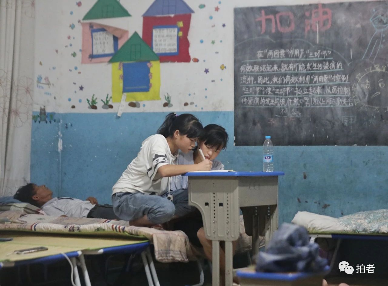 △ 7月10日晚,鄱陽縣油墩街鎮橋頭中心小學安置點,黃先生躺在牀上閉目養神,雙胞胎孫女正在做暑假作業。