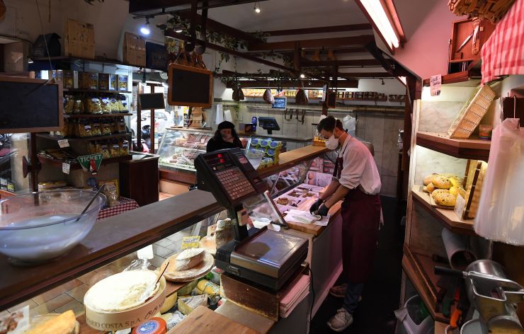 图为19日,意大利罗马,一家食品店的员工戴着口罩工作。(图片来源:新华社)